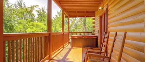A wooden deck with a hot tub and seating area, overlooking a forested area.