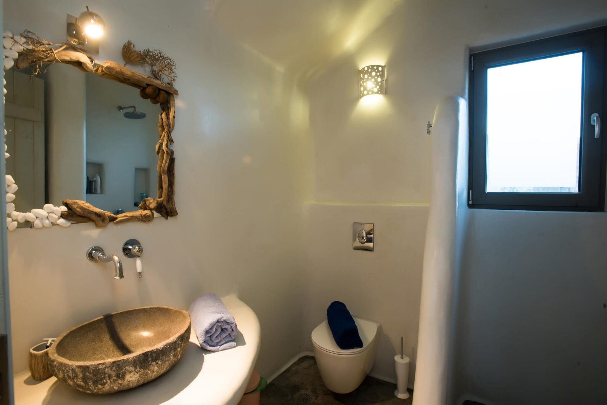 Une salle de bain avec un lavabo en pierre, un miroir, des toilettes et une fenêtre.