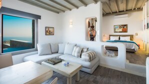 Ein modernes Wohnzimmer mit großem Fenster, einer Couch, einem Couchtisch und einem Bett mit Blick.