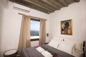 A hotel room with a bed, a view of the sea, and a painting on the wall. - Divine Mykonos Villa Ananke, 4 BDR, Private Pool & Plunge Pool, Sea Views (Mykonos)