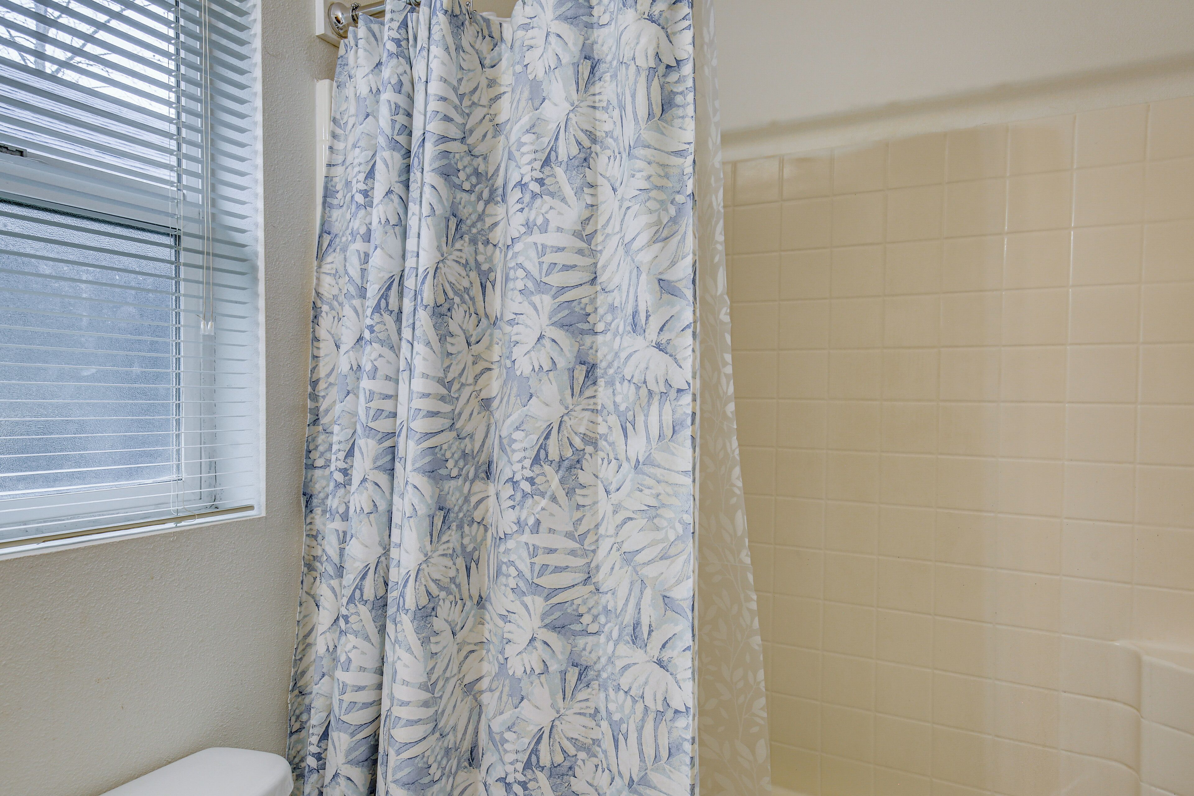 A bathroom with a toilet, a shower curtain with a floral pattern, and a tiled wall.