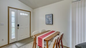 Ein Essbereich mit einem Holztisch, weißen Stühlen, einer rot-weißen Tischläufer und einem gerahmten Bild an der Wand.