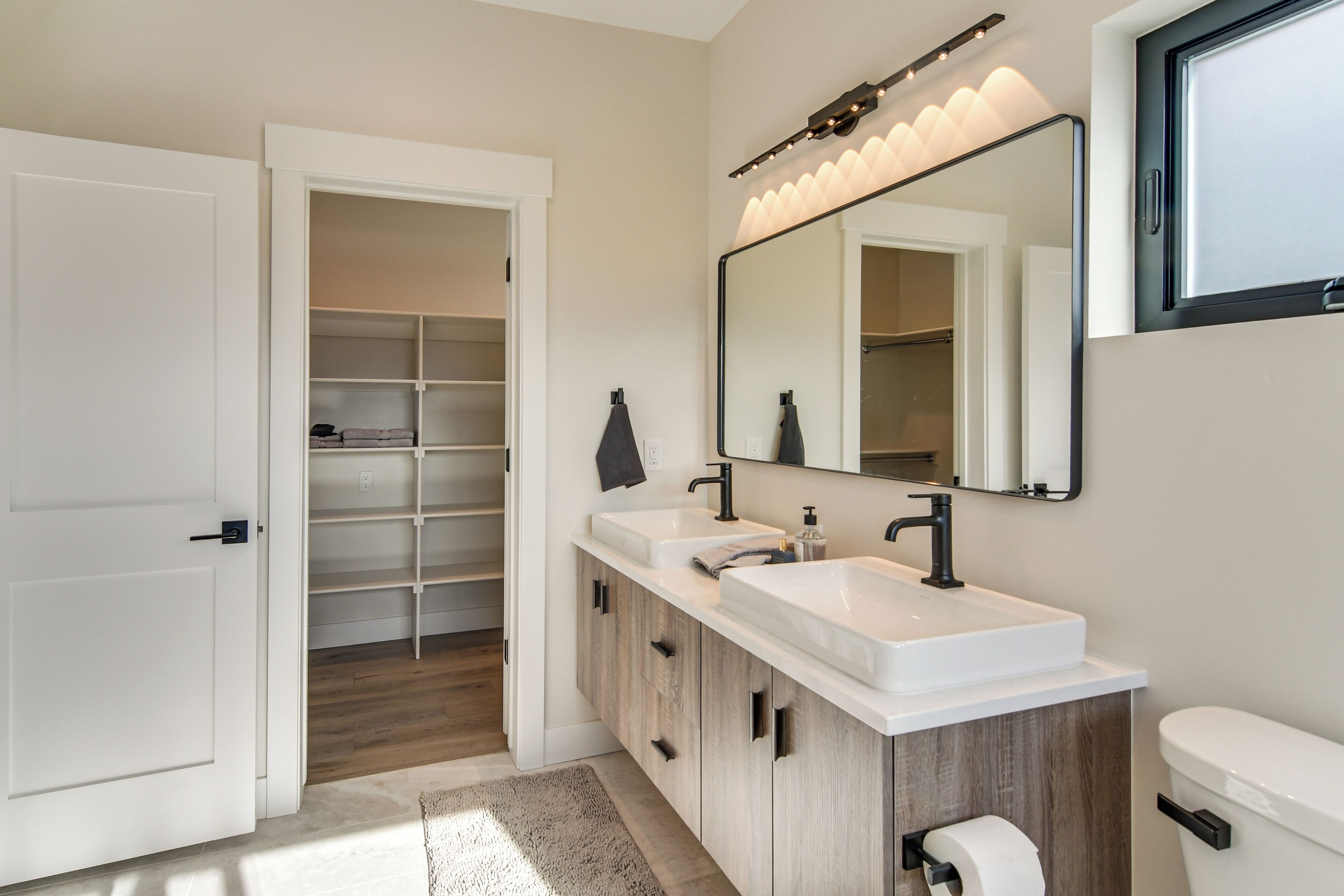 A modern bathroom with two sinks, a large mirror, and a walk-in closet.