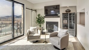 Ein modernes Wohnzimmer mit Kamin, großem Fernseher und Glastür zum Balkon.