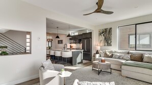 Ein modernes Wohnzimmer mit einer Couch, einem Sessel und einem Couchtisch, einer Küchenzeile mit Barhocker und einem Esstisch.