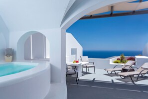 Un espacio exterior moderno con techo blanco, piscina, sillas de descanso y una mesa con vistas al mar.