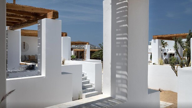 Un complex turístic modern amb parets blanques, una pèrgola de fusta i una escala que condueix a una zona coberta.
