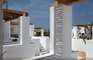 A modern resort with white walls, a wooden pergola, and a staircase leading to a covered area. - Suite Virelya, Furnished Terrace, Naousa (Paros)