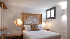 Un dormitori amb un llit gran, un panell de capçal de fusta, làmpades laterals i una finestra amb cortines.