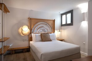 Une chambre à coucher avec un grand lit, une tête de lit en bois, des lampes de chevet et une fenêtre avec des rideaux.