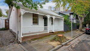 A white two-story house with a front porch, a wooden front door, and a mailbox. - Draper Garden Cottage with Parking (South Melbourne)