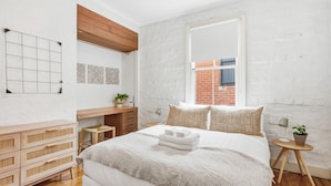 A bedroom with a bed, wooden dresser, desk, and a window with a view of a brick building. - The Albert Park Pocket - Stylish Stay with Parking (South Melbourne)