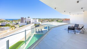 Eine Dachterrasse mit Glasgeländer, einem Pool und einer Sitzgelegenheit mit zwei Stühlen und einem Tisch.