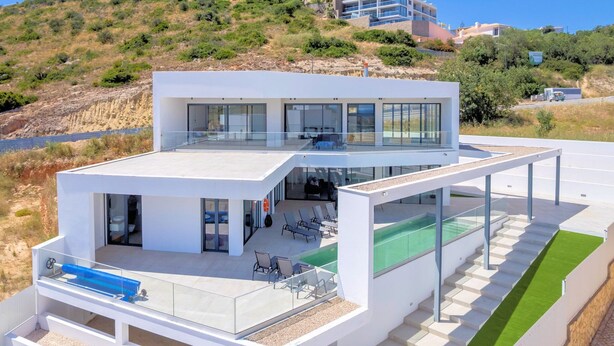 Ein modernes, zweistöckiges Haus mit Glasbalkon, Schwimmbad und Blick auf die umliegende Landschaft.