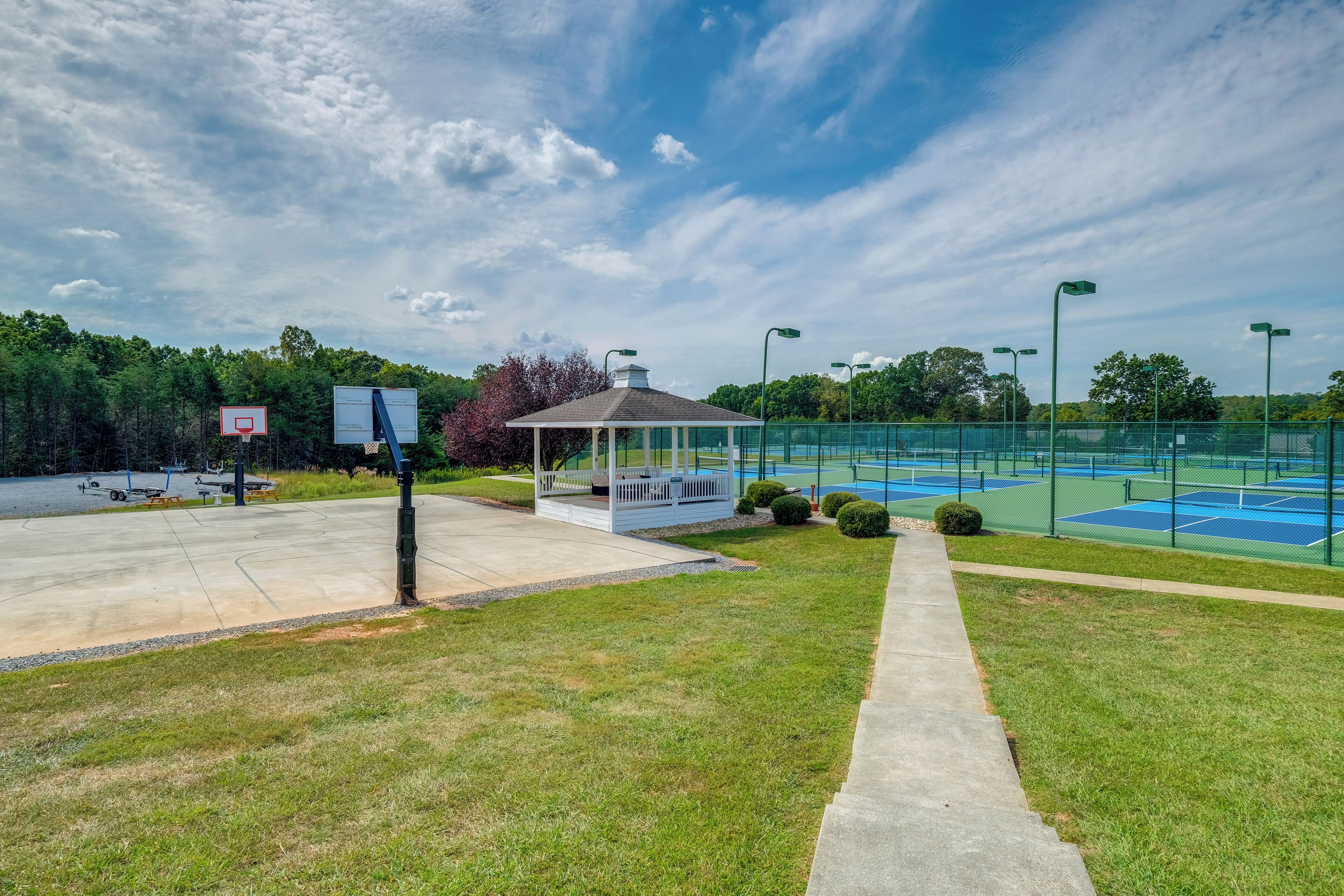 A tennis court with a pavilion, a basketball hoop, and a covered seating area.
