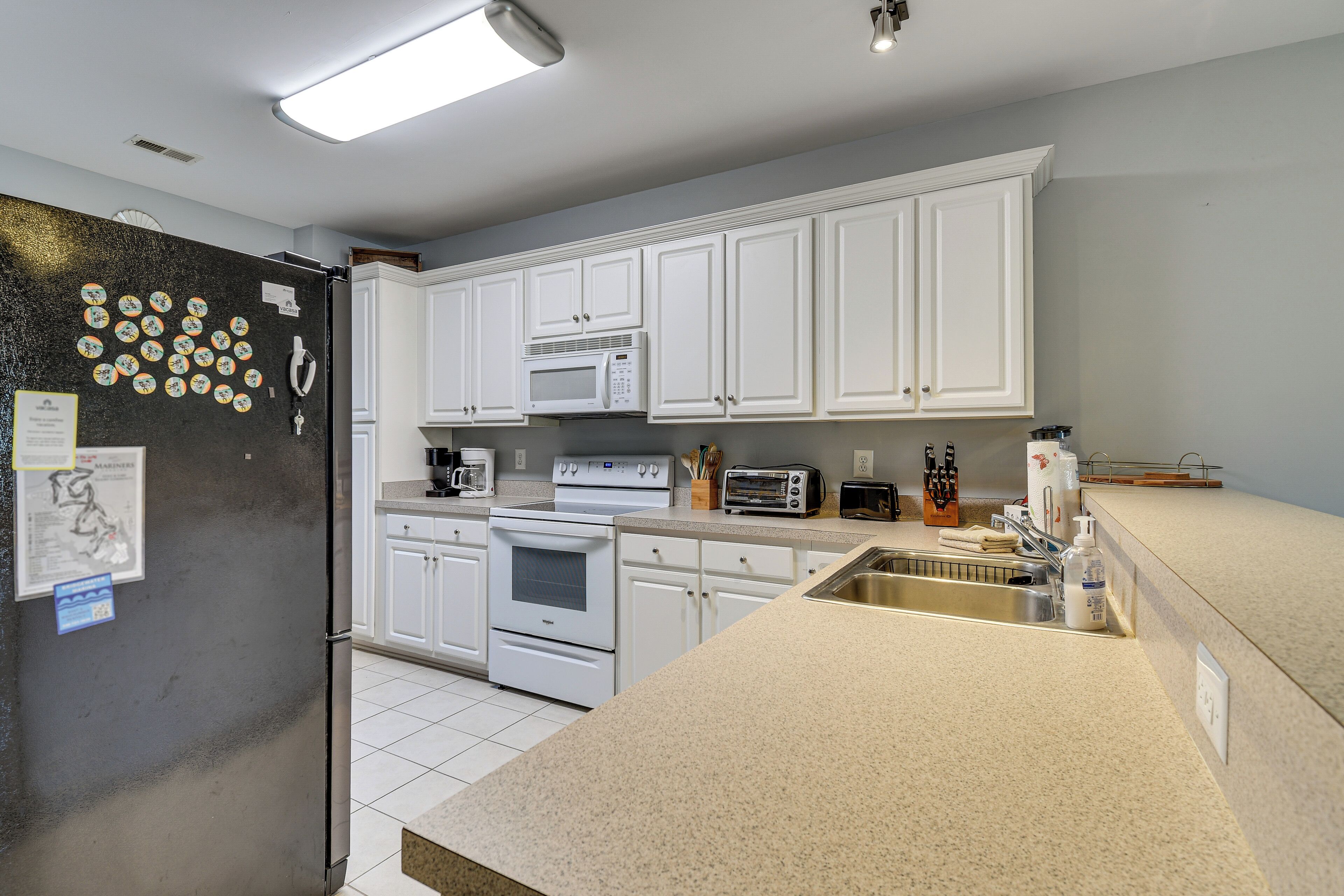 A modern kitchen with white cabinets, a stainless steel refrigerator, a microwave, a toaster, and a sink.
