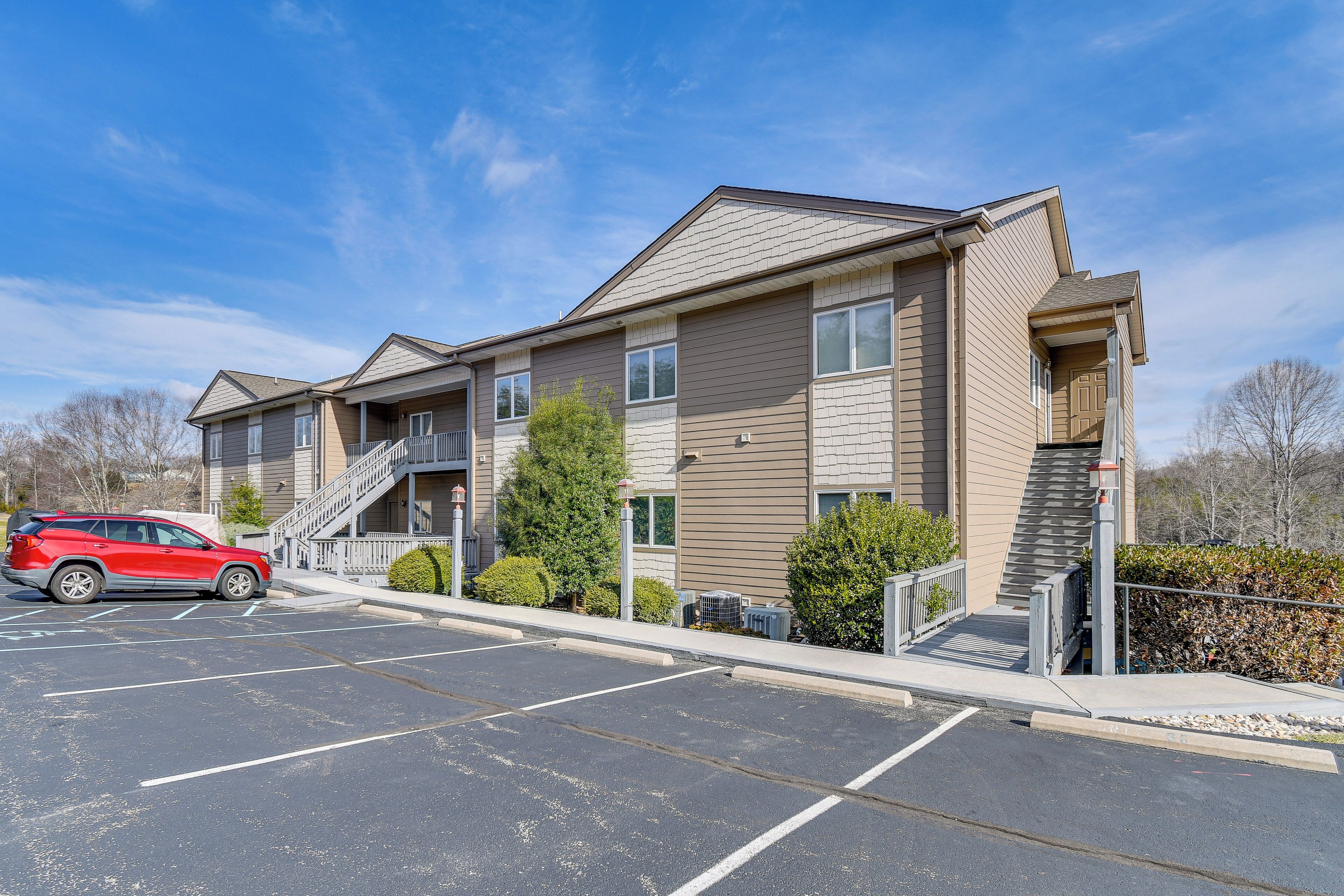 Un immeuble d’appartements à plusieurs étages, avec un parking, un SUV rouge et un escalier menant à l’entrée.