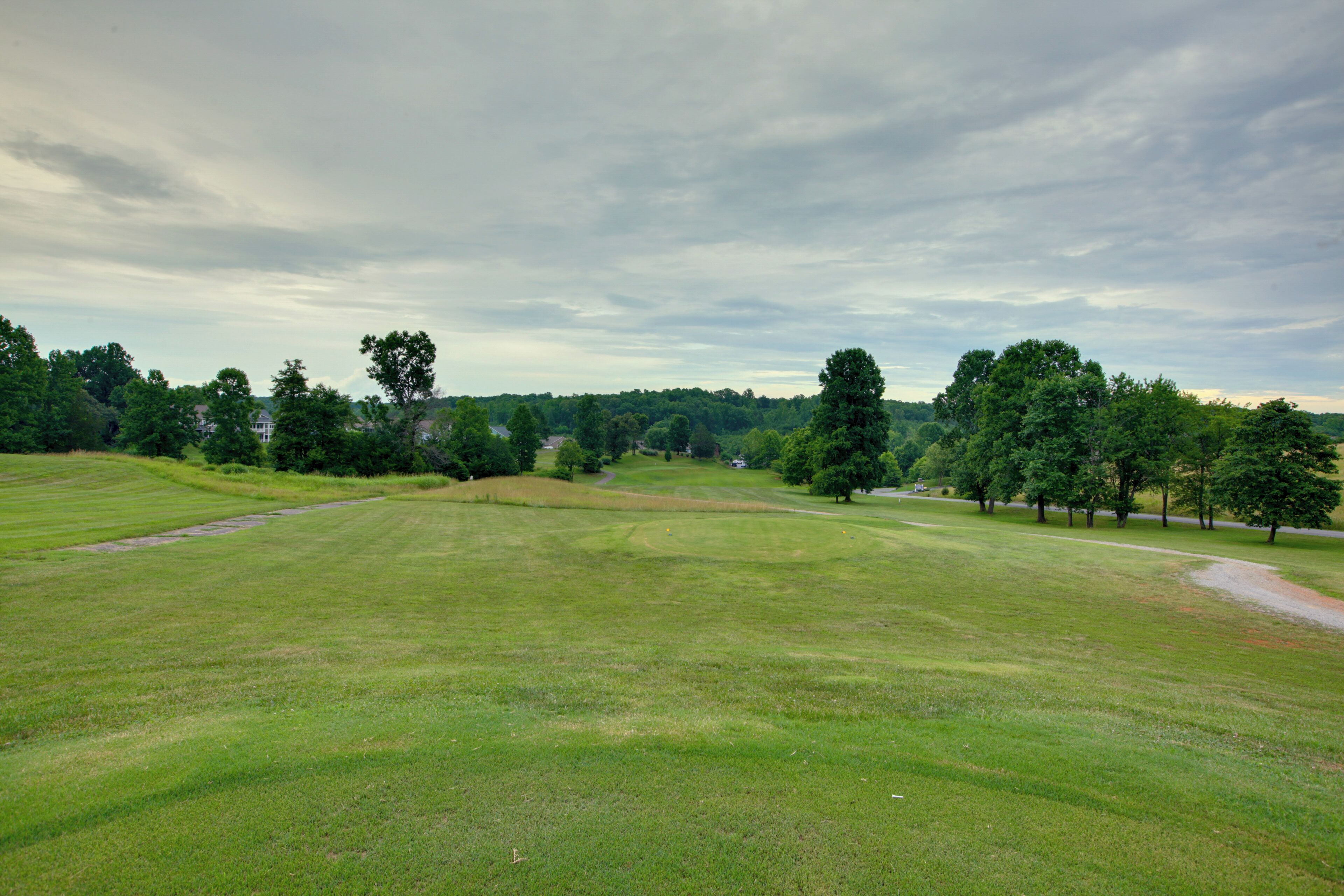 A wide, open grassy field with scattered trees and a distant building.