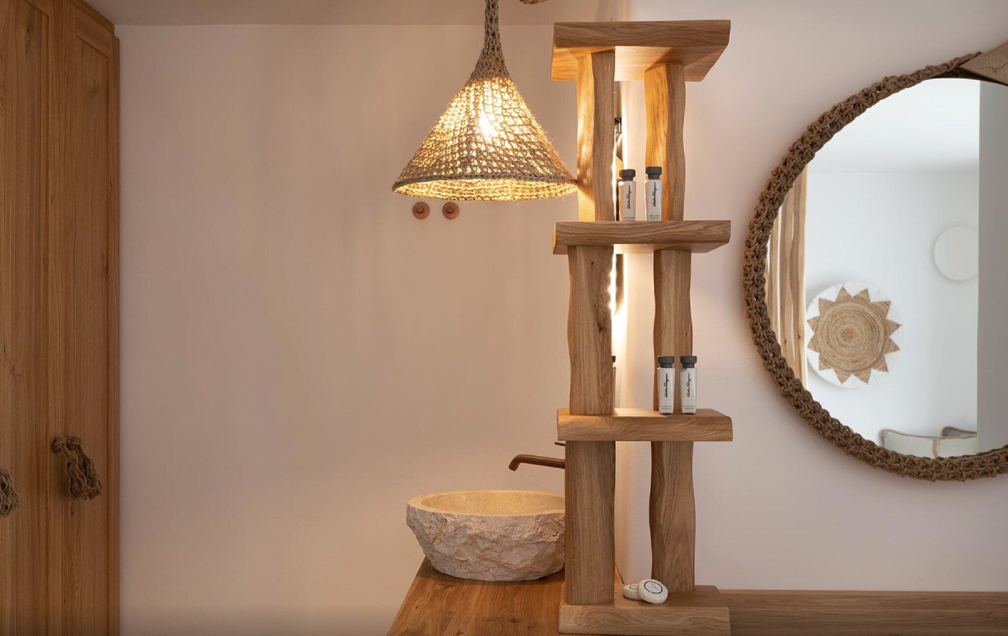 Une étagère en bois, un luminaire suspendu, un lavabo en pierre et un miroir avec un cadre tressé.