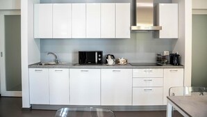 A modern kitchen with white cabinets, a stainless steel range hood, a microwave, and a coffee maker.