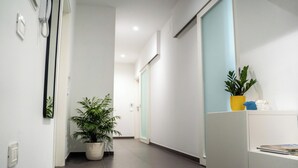 A hallway with a potted plant, a white reception desk, and a door in the background.