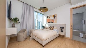 A modern hotel room with a large bed, a desk, a chair, a TV, and a shower area. - Dubai Mall Apt w/ Burj Khalifa & Fountain Views (Dubai)