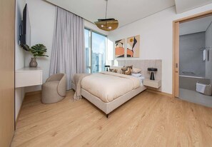 A modern hotel room with a large bed, a desk, a chair, a TV, and a shower area. - Dubai Mall Apt w/ Burj Khalifa & Fountain Views (Dubai)