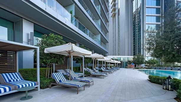 A modern hotel with a poolside area featuring lounge chairs and umbrellas, a clear view of the pool, and a contemporary building facade. - Dubai Mall Apt w/ Burj Khalifa & Fountain Views (Dubai)