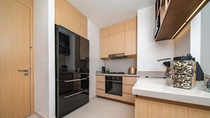 A modern kitchen with wooden cabinets, a black refrigerator, a stove, and a coffee maker. - Dubai Mall Apt w/ Burj Khalifa & Fountain Views (Dubai)