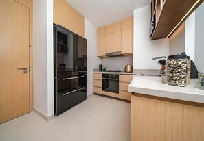 A modern kitchen with wooden cabinets, a black refrigerator, a stove, and a coffee maker. - Dubai Mall Apt w/ Burj Khalifa & Fountain Views (Dubai)