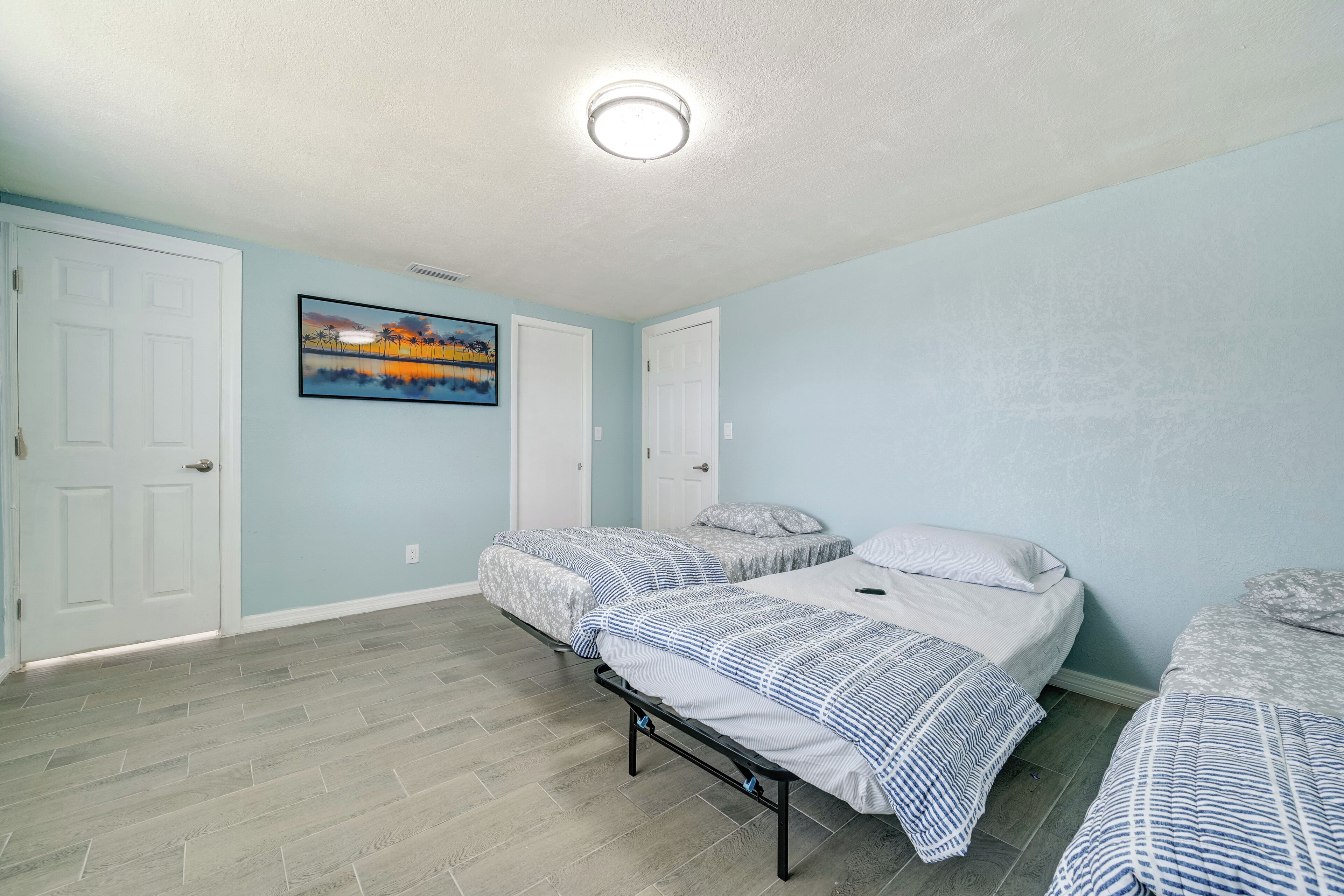 A bedroom with two beds, light blue walls, and a painting on the wall.
