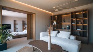 A modern living room with a sofa, a coffee table, and built-in shelves with decorative items. - Rhethis Suite, Divine Sea Views, Infinity Pool, Oia (Santorini)