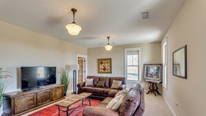 A living room with a large flat-screen TV, leather sofas, a wooden entertainment unit, and a red carpet. - Peaceful, Serene Getaway 17 Mi to Dtwn Roswell! (Roswell)