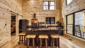 Ein Holzhütten-Interieur mit Küche, Barhocker und großen Fenstern.