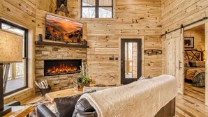 Ein gemütliches Blockhaus-Interieur mit Kamin, Holzwänden, einer Couch und einem Fernseher.