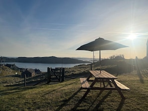 A picnic table and umbrella by a lakeside with a clear view of the water and distant hills.