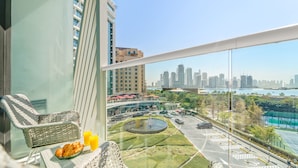 A balcony with wicker furniture, a bowl of croissants, and a glass of orange juice. A cityscape with high-rise buildings and a body of water is visible in the background. - Seven Palm - 206 Studio (Dubai)