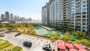 A high-rise building with multiple balconies, a parking lot, and a tennis court. - Seven Palm - 206 Studio (Dubai)