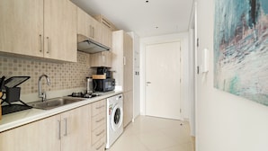 A modern kitchen with light wood cabinets, a stainless steel sink, a microwave, and a washing machine. - Seven Palm - 206 Studio (Dubai)