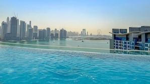 A waterfront view of a cityscape with modern buildings, a large body of water, and a bridge in the distance. - Seven Palm - 206 Studio (Dubai)