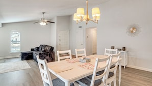 A dining area with a white table, chairs, and a chandelier. There is a ceiling fan, a door, and a wall clock. - DFW Home Base! Quiet Suburb Stay w/ Yard (Carrollton)