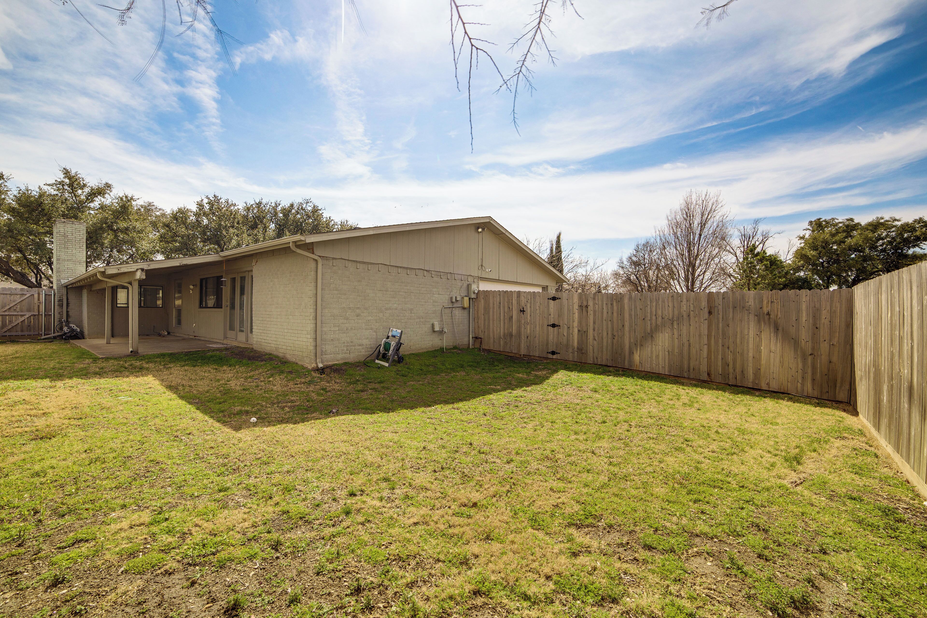 A single-story house with a detached garage, a fenced backyard, and a clear sky.
