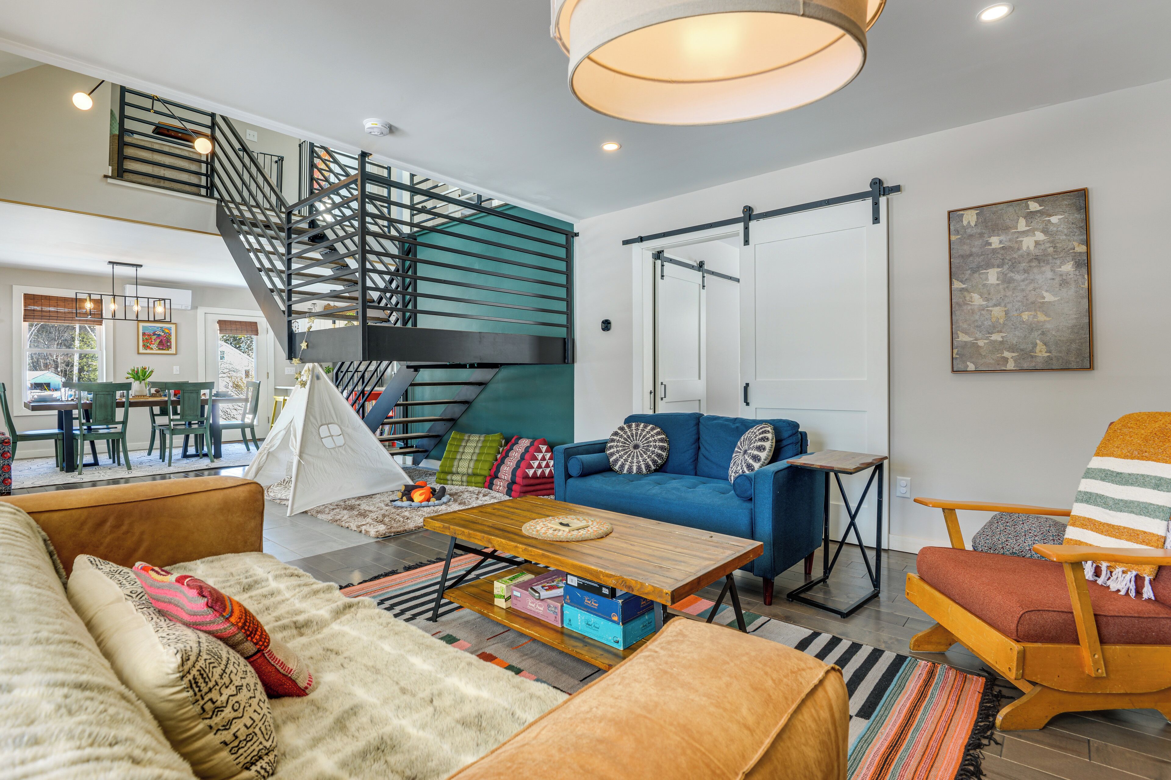 Ein modernes Wohnzimmer mit Treppe, einem blauen Sofa, einem Holztisch und einem gestreiften Sessel.