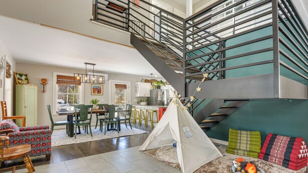 Un vaste espace de vie doté d’un haut plafond, d’un escalier, d’un coin repas et d’un espace douillet aménagé avec une tente et des coussins.