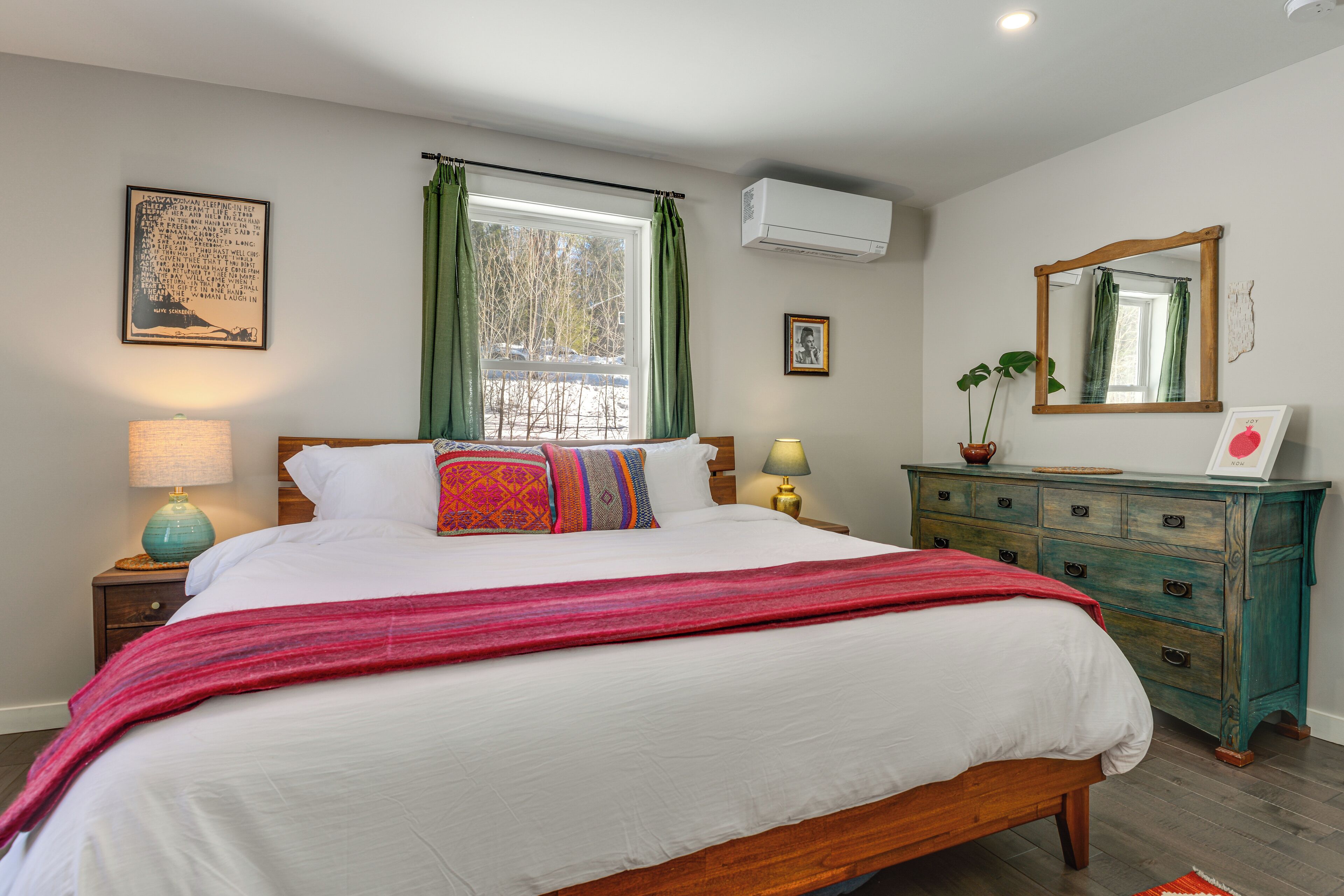 A bedroom with a large bed, a dresser, a mirror, and a window with curtains.