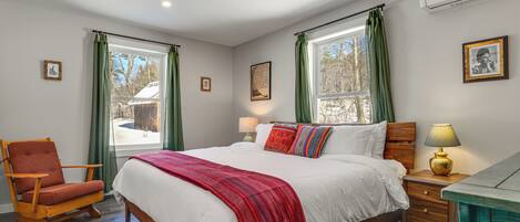 A bedroom with a wooden bed, green curtains, a red throw blanket, a wooden nightstand, and a chair.