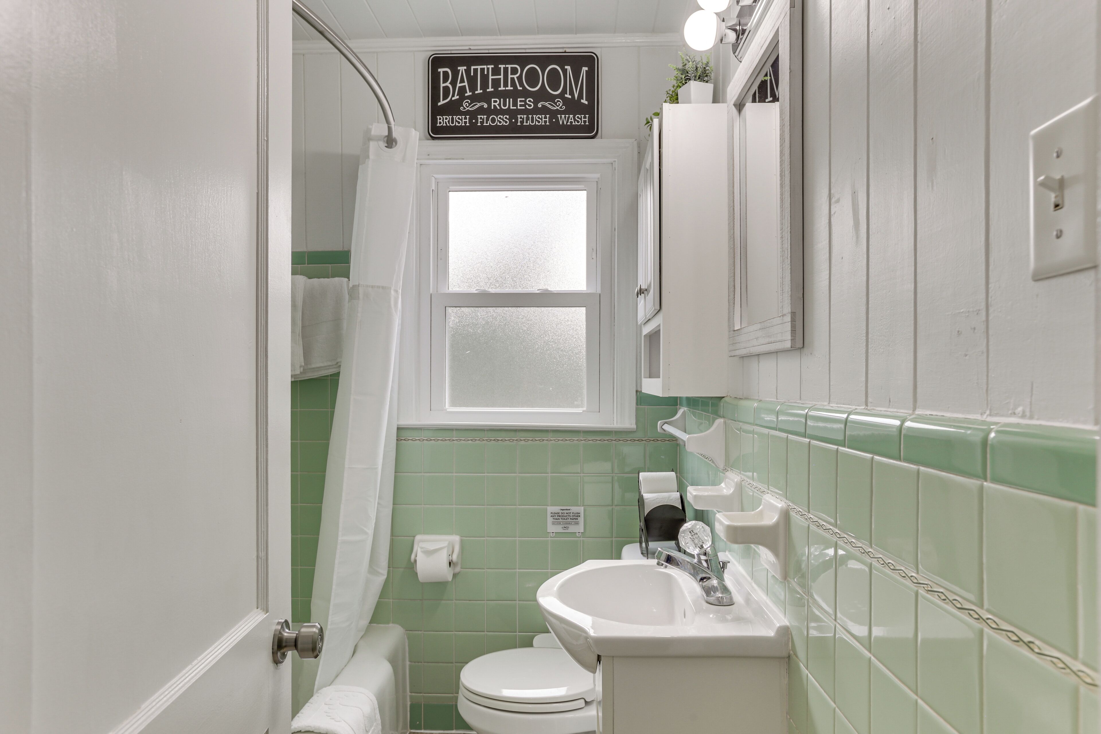 A bathroom with a sign listing bathroom rules, a toilet, a sink, and a shower area.