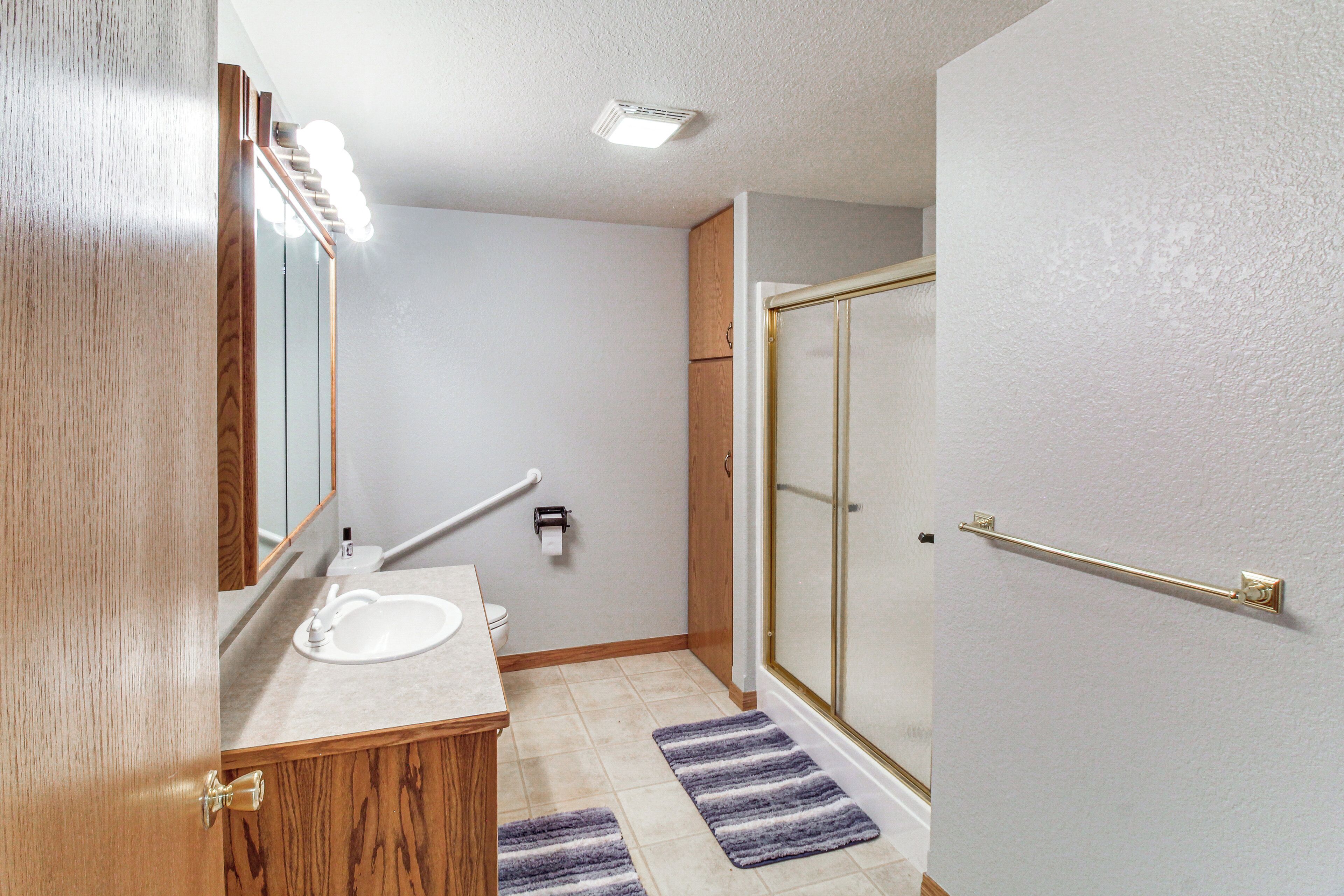A bathroom with a wooden vanity, a sink, a mirror, a towel rack, a shower with a glass door, and a toilet.