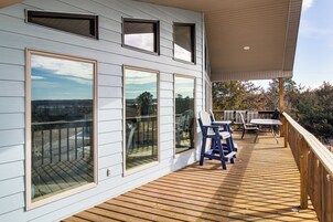 Una terraza de madera con mobiliario exterior, ventanas amplias y una zona cubierta.