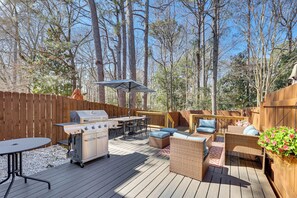 Eine Holzterrasse mit Grill, Esstisch und Korbmöbeln.